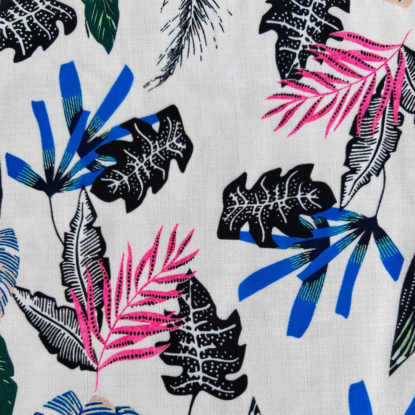Close-up of fabric: A men's Aloha Hawaiian button-down shirt on a model. The shirt is multicolored on an off-white background with highlights of green, pink, blue, and dark brown. It has a plant and leaf pattern.
