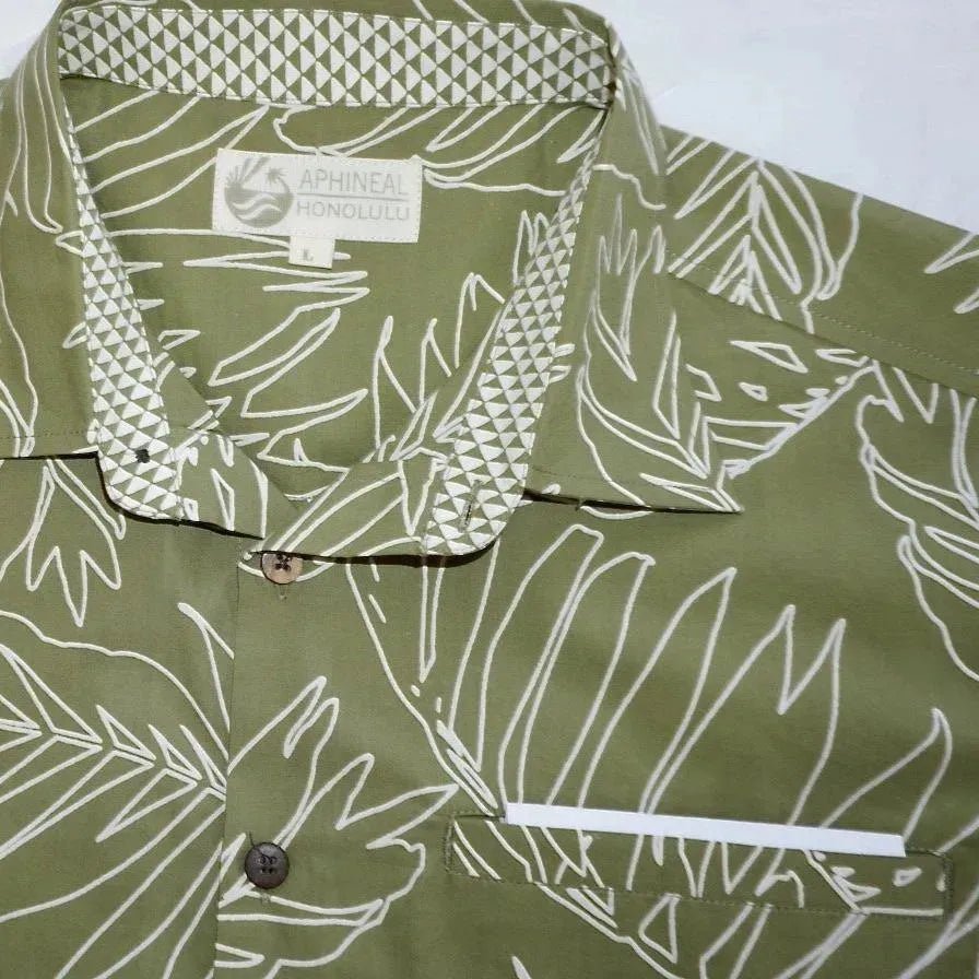 Shown on a flat surface and close-up to the collar, is a green aloha Hawaiian button-down shirt with a palm leaf pattern design. Made by Phin Hawaii.