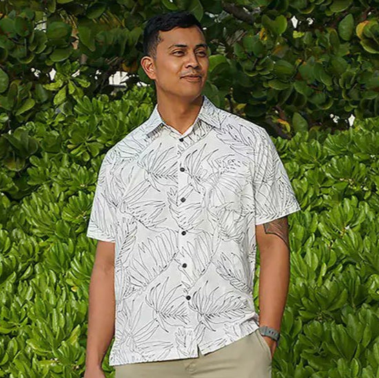 A man modeling a white aloha Hawaiian button-down shirt with a palm leaf pattern design. Made by Phin Hawaii.